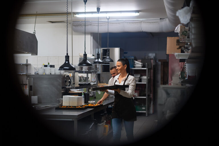 A happy chef and cook working on their dishes in restaurant kitchen, shot through circle door window. From Kitchen to Courtroom: How Surveillance Footage is Transforming the Restaurant Industry