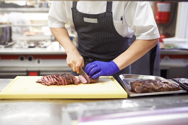 Hands, chef and cutting steak for restaurant with catering industry, board and fine dining for nutrition. Employee, knife and beef in industrial kitchen for hospitality, dinner and cooking career. CRMBC discusses Restaurant Safety Loss Control with Path Alliance.