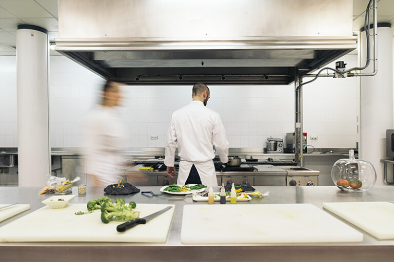 Chef cooks working in professional kitchen. Chefs hurry up, actively cooking meals for restaurant. Long exposure with motion blurred figures